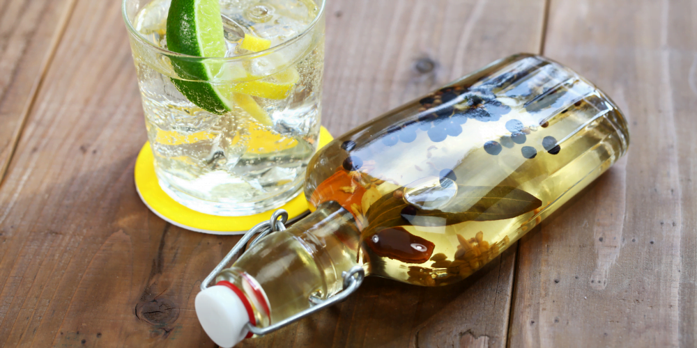 Bottle of infused gin on its side, next to a glass with lemon and lime