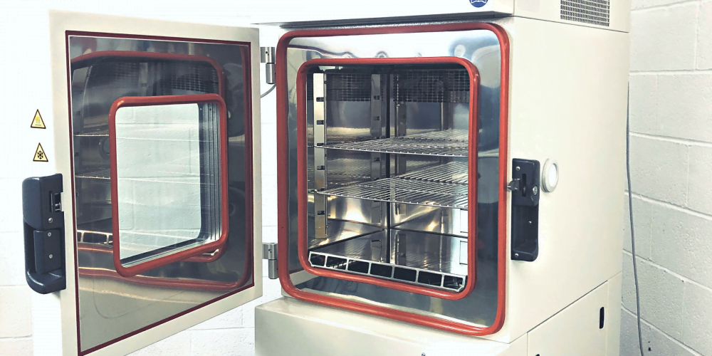 Inside of climatic chamber. Chamber has two shelves, red seals, and viewing window