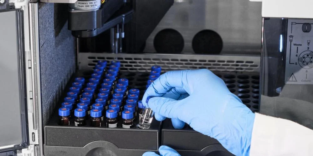 Close up woman hand in a rubber gloves put sample in a glass vial with blue cap into the autosampler rack in HPLC system. High performance liquid chromatography for separation compounds