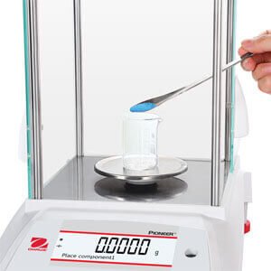 Scientist placing blue powder sample onto an analytical balance